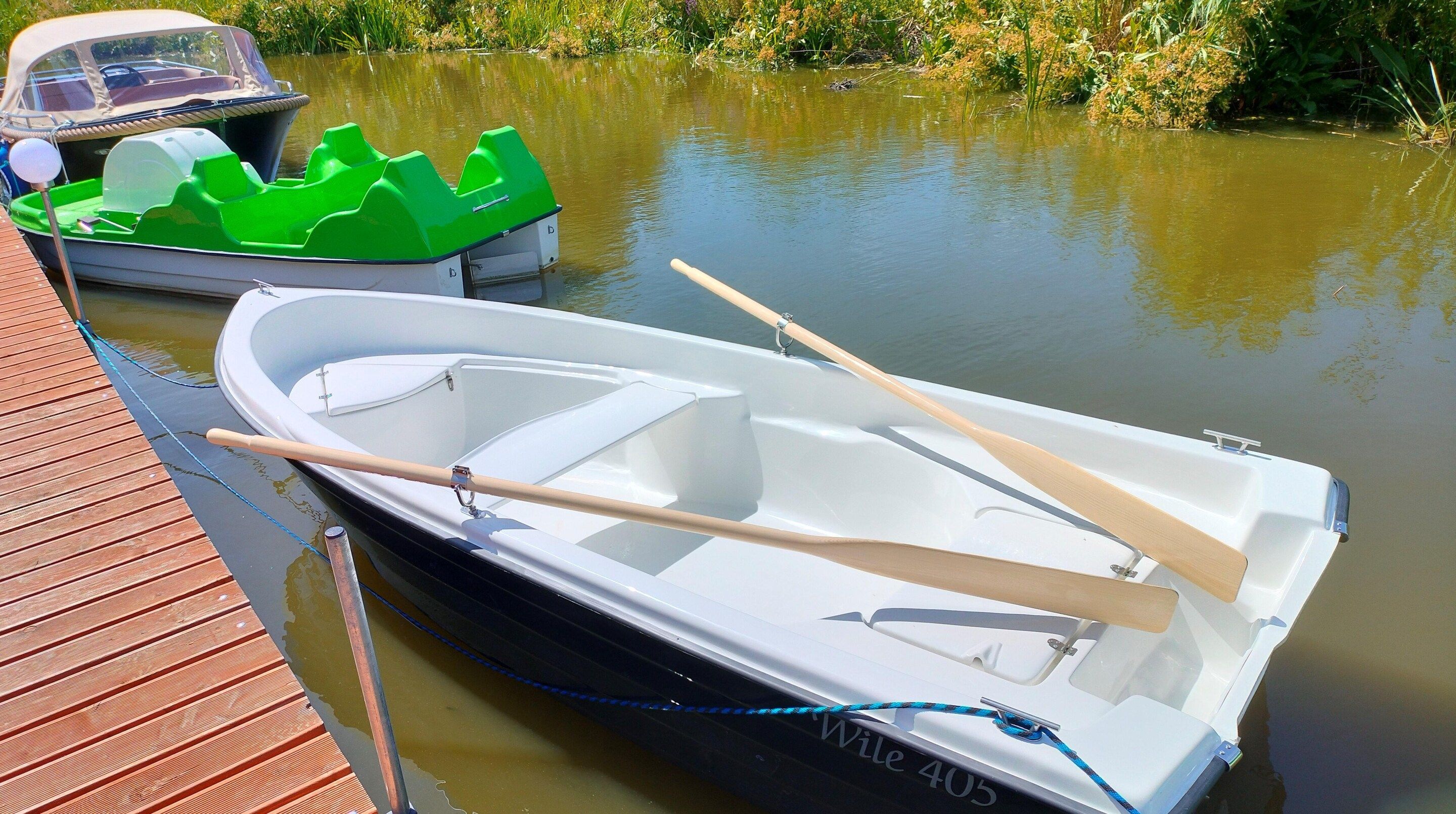 A small white rowboat with oars and a green inflatable boat docked at a wooden pier.