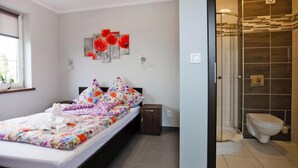 A bedroom with a bed, a bedside table, a wall-mounted artwork, and a bathroom with a toilet and a shower. - Comfortable Ground Floor Apartment, Summer Pool (Mielno)