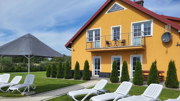 A yellow building with a red roof, white windows, and a balcony with outdoor furniture. - Comfortable Ground Floor Apartment, Summer Pool (Mielno)