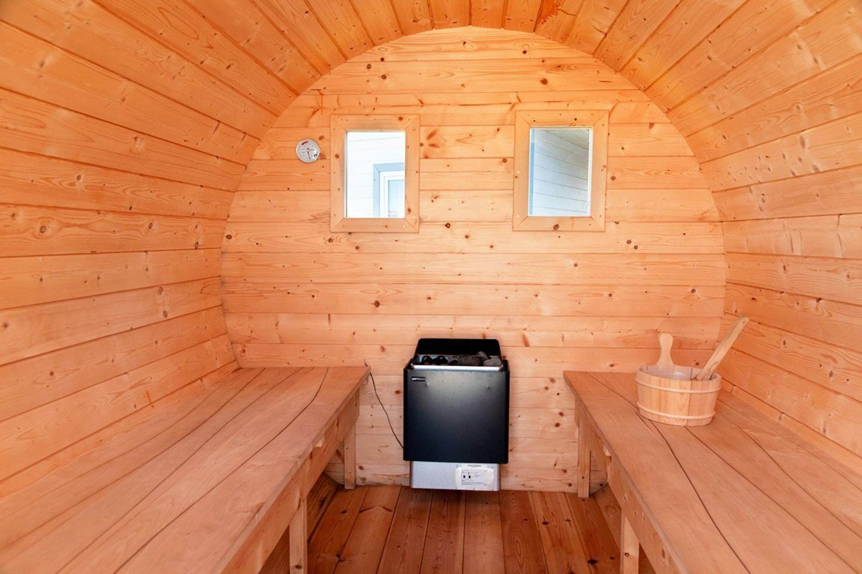 A wooden sauna room with benches, a sauna unit, and a wooden bucket.