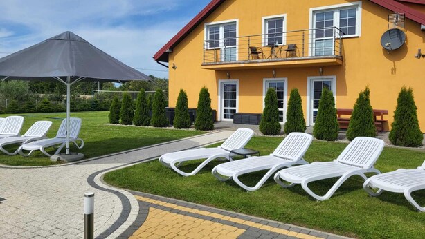A yellow building with a red roof, a balcony with outdoor furniture, and white lounge chairs arranged on the lawn. - Comfortable Ground Floor Apartment, Summer Pool (Mielno)