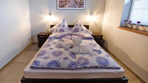 Un letto rifatto con cura, con una coperta a motivi e cuscini, due comodini con lampade, un quadro appeso alla parete e una finestra con persiane.