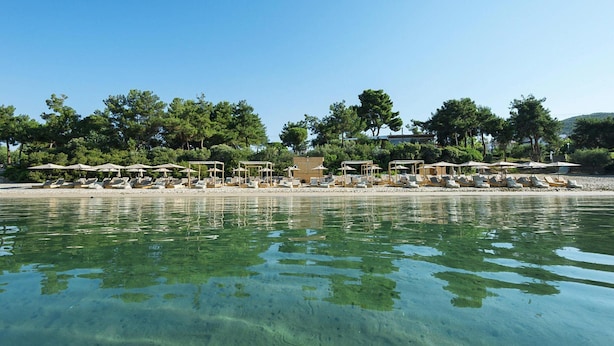 Hotel a la vora d'una platja amb aigua cristal·lina, ombrel·les i gandules.