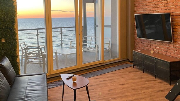 A modern living room with a large glass door leading to a balcony overlooking the sea. - Apartment in Dziwnowek Near the Beach (Dziwnów)