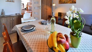 A dining area with a table set for two, a bowl of fruit, a bottle of olive oil, and a potted orchid. - Comfortable Holiday Apartment, air Conditioning (Ustronie Morskie)