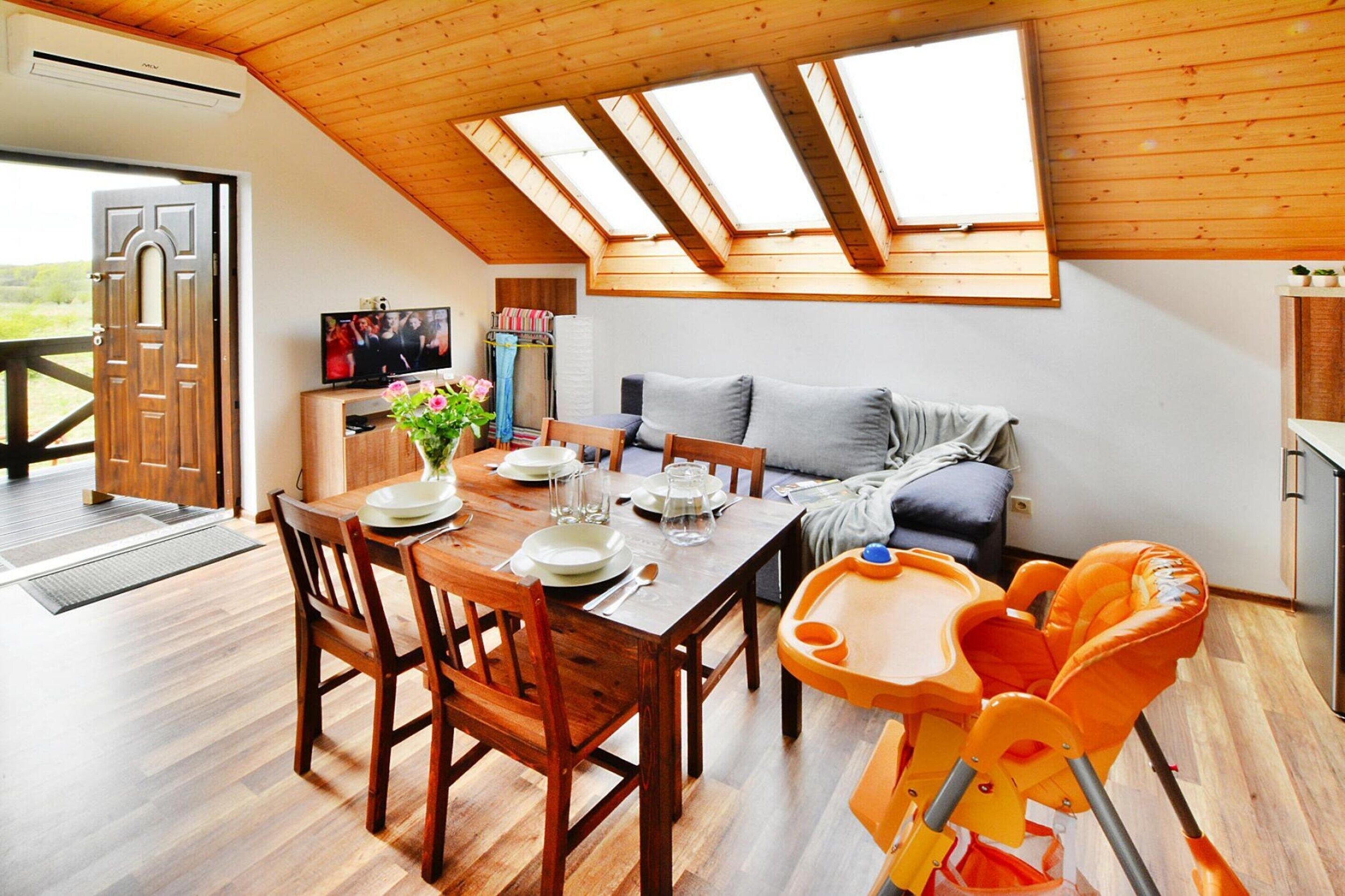 Un espace repas avec une table et des chaises en bois, un plafond haut doté de fenêtres de toit et une vue sur l’extérieur.