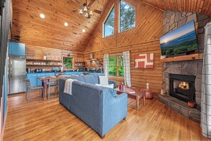 A spacious living area with a fireplace, wooden ceiling, and a large window.