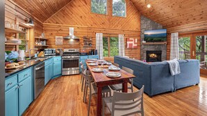 A log cabin interior with a dining area, kitchen, and living room, featuring wooden floors, a fireplace, and large windows. - Cabin On 8-Private Acres, Hot Tub, Game Room, Views (Bryson City)