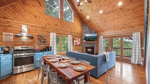 A wooden cabin interior with a dining table, kitchen, and fireplace. - Cabin On 8-Private Acres, Hot Tub, Game Room, Views (Bryson City)