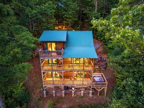 A multi-level log cabin with a green roof, multiple decks, and a hot tub.