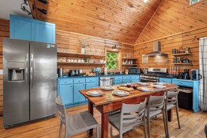 A wooden cabin kitchen with a central island, stainless steel refrigerator, blue cabinets, and a dining table set for four.