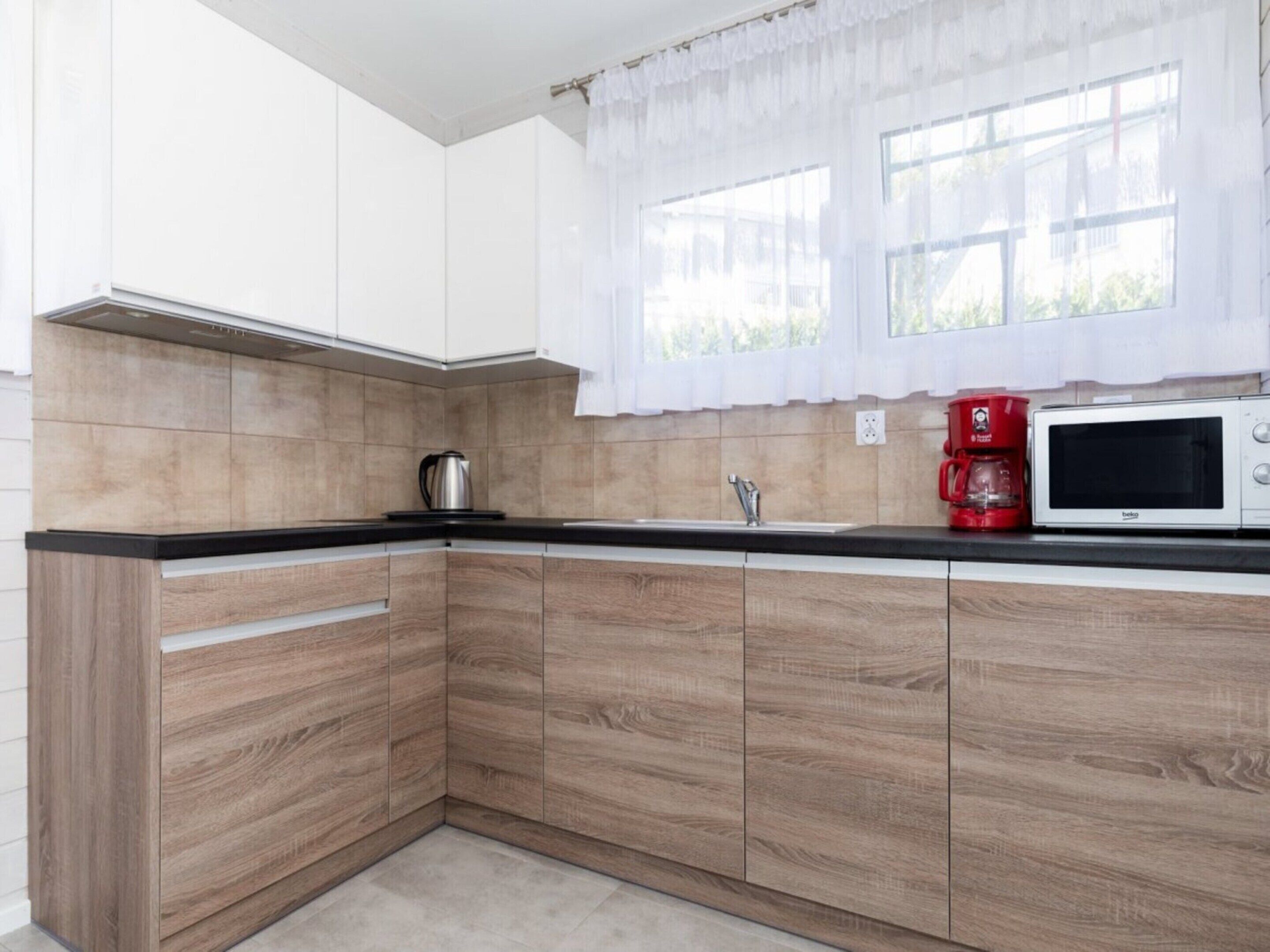 A modern kitchen with wooden cabinets, a black countertop, a kettle, a red coffee maker, and a microwave.