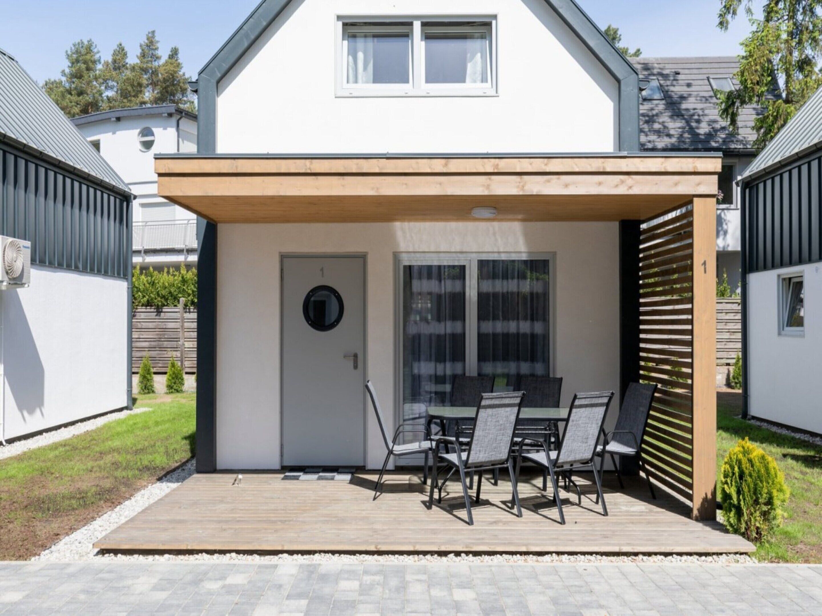 A modern house with a covered patio, a dining table with chairs, and a small garden area.