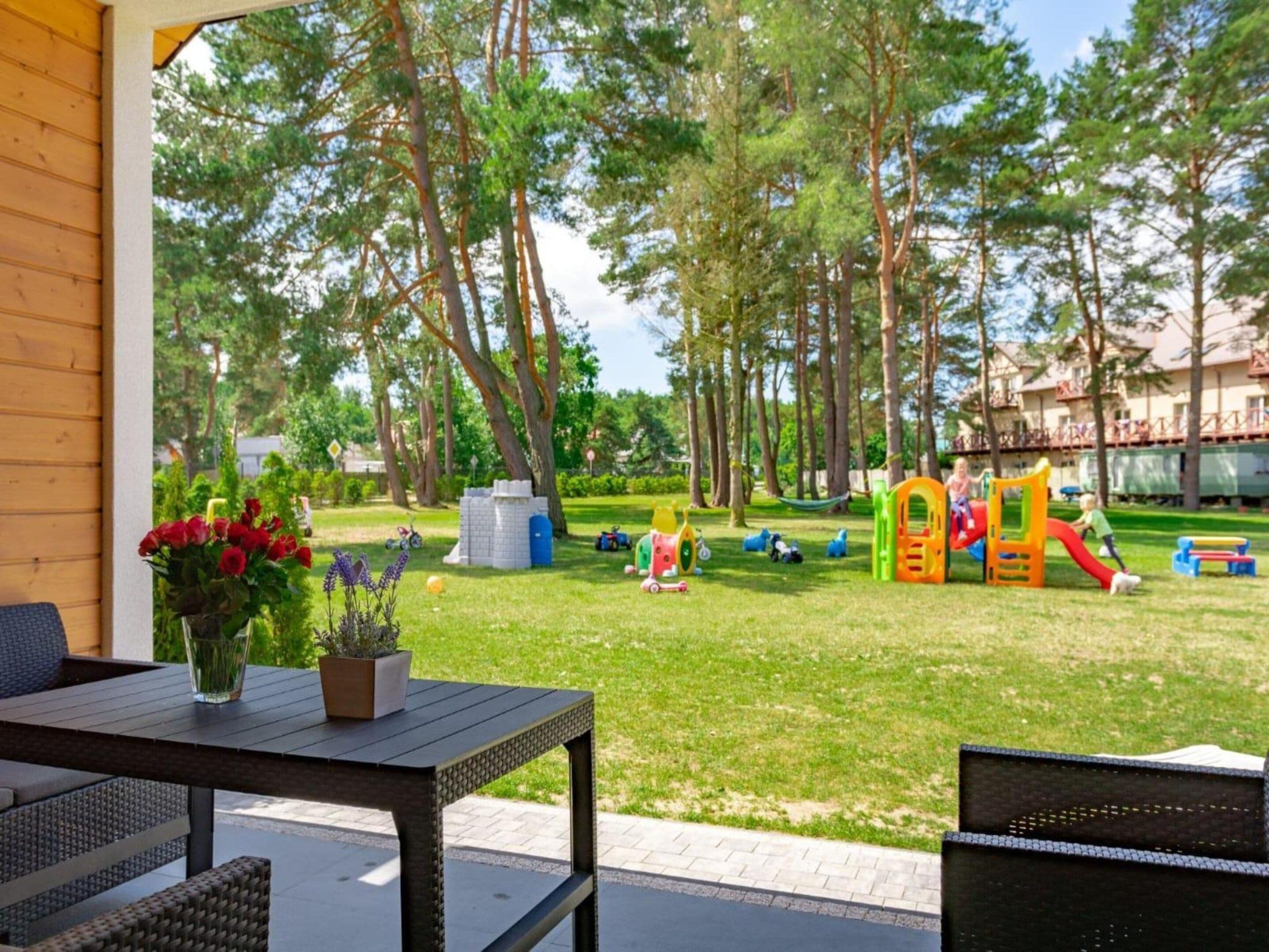A patio area with outdoor furniture, a play area with colorful playground equipment, and a view of a wooded area.