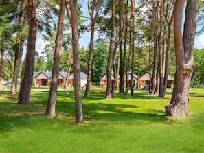 A campground with multiple cabins surrounded by tall trees and grassy areas. - Comfortable Holiday Homes, Large Garden (Postomino)