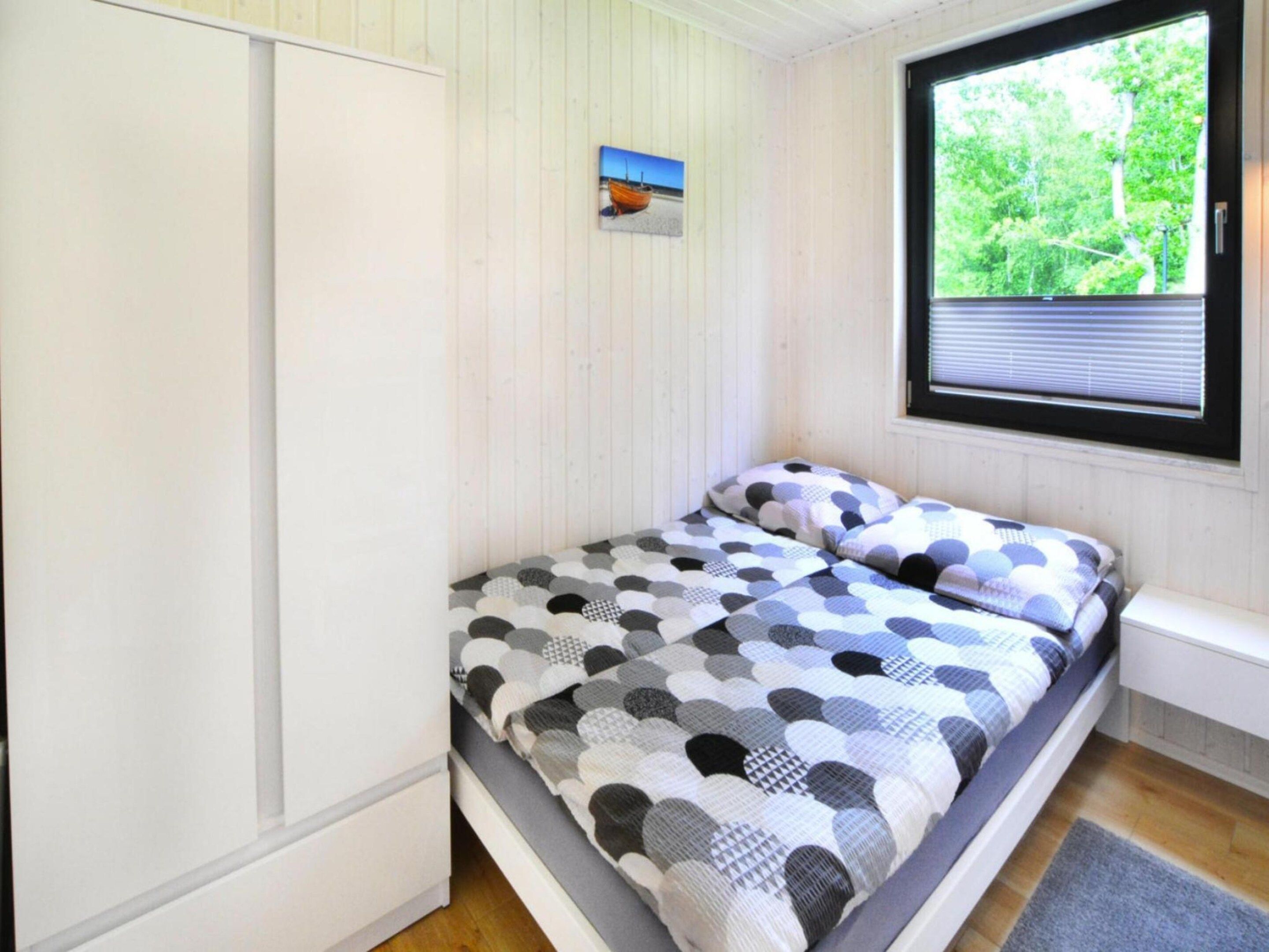 A bedroom with a bed, a window with blinds, a picture on the wall, and a door.