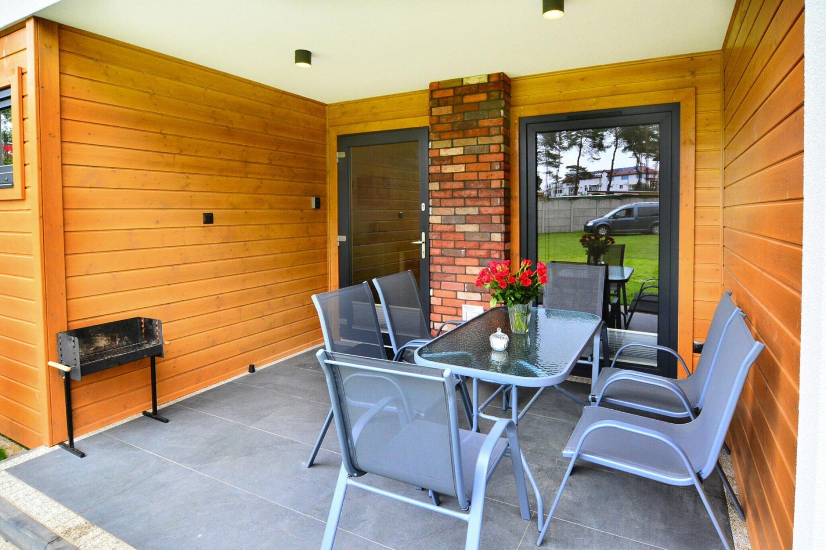 An outdoor patio with a glass table and metal chairs, a brick pillar, and a wooden wall.
