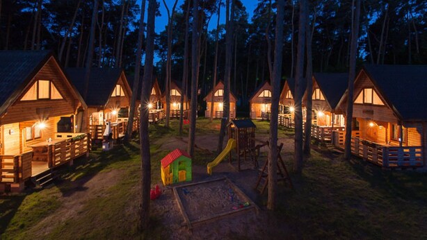 A row of wooden cabins with attached porches, surrounded by tall trees. - Apartment in Pobierowo Near Baltic Sea Beach (Rewal)