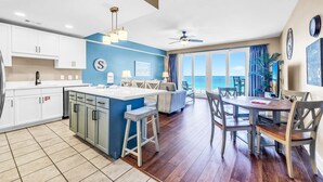 A modern kitchen with white cabinets, a blue accent wall, a central island with stools, and a dining area with a table and chairs.