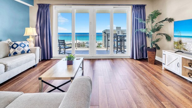 A modern living room with a large sliding glass door leading to a balcony with a view of the beach and ocean.
