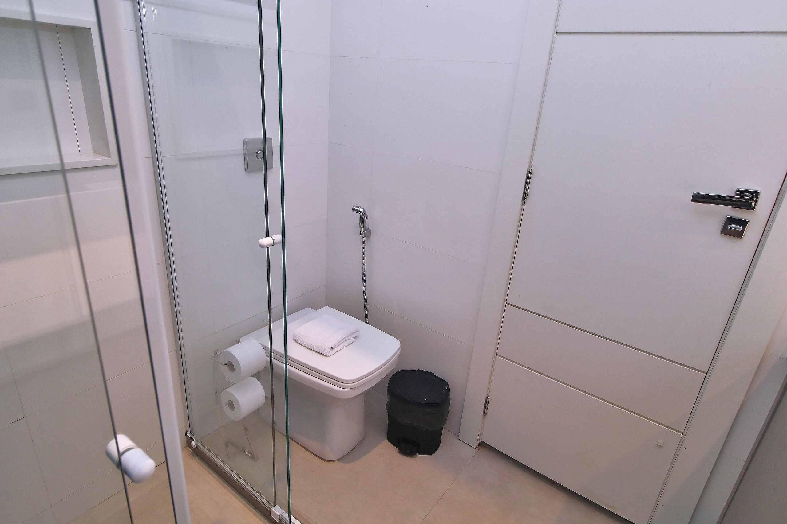 Un baño pequeño y moderno con cabina de ducha de vidrio, inodoro blanco y un bote de basura negro.