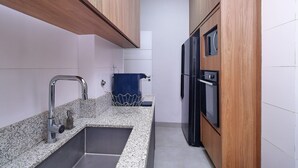 A kitchen with granite countertops, stainless steel sink, wooden cabinets, and a black refrigerator. - D055 (Rio de Janeiro)