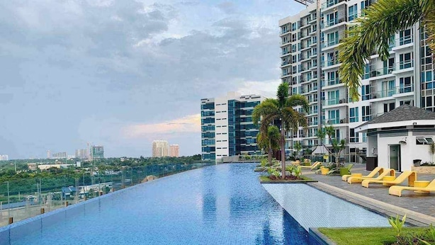 A rooftop infinity pool with a view of the city skyline, surrounded by modern buildings and palm trees. - Cozy 1 Bedroom in Mactan Newtown (Lapu-Lapu)