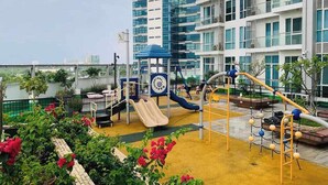 A playground with slides and climbing structures, surrounded by a fence and greenery. - Cozy 1 Bedroom in Mactan Newtown (Lapu-Lapu)