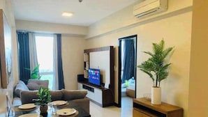 A modern living room with a sofa, a dining table set for four, a flat-screen TV, and a potted plant. - Cozy 1 Bedroom in Mactan Newtown (Lapu-Lapu)