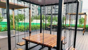 A covered outdoor seating area with wooden tables and benches, surrounded by a chain-link fence and greenery. - Cozy 1 Bedroom in Mactan Newtown (Lapu-Lapu)