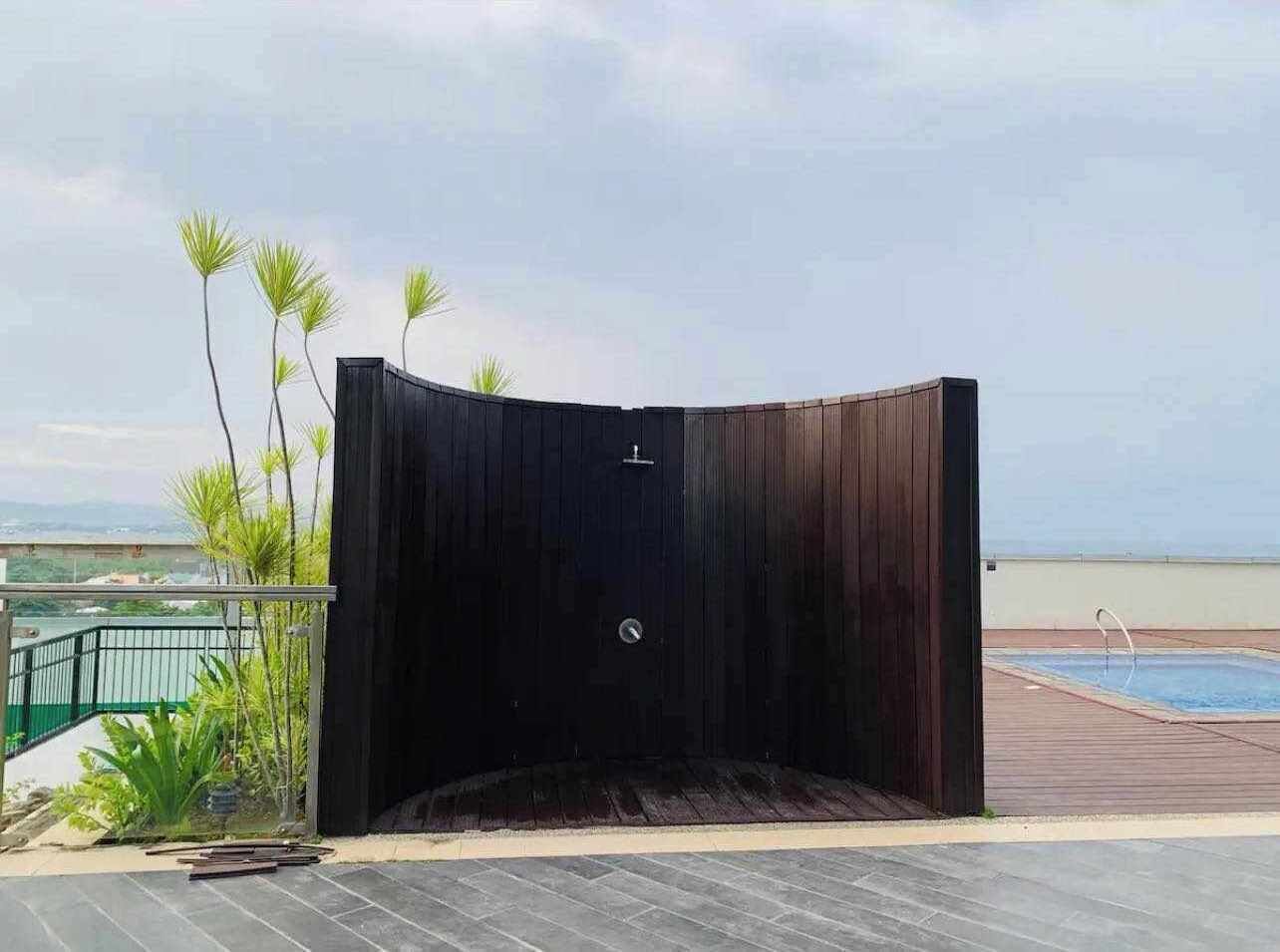 Una estructura de madera con una puerta, rodeada por una zona de piscina y plantas.