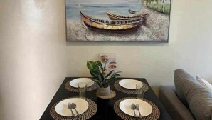 A dining table set for four with a tropical painting above it. - Cozy 1 Bedroom in Mactan Newtown (Lapu-Lapu)