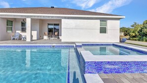Una casa moderna con piscina, un patio con sillas y un cielo azul despejado.