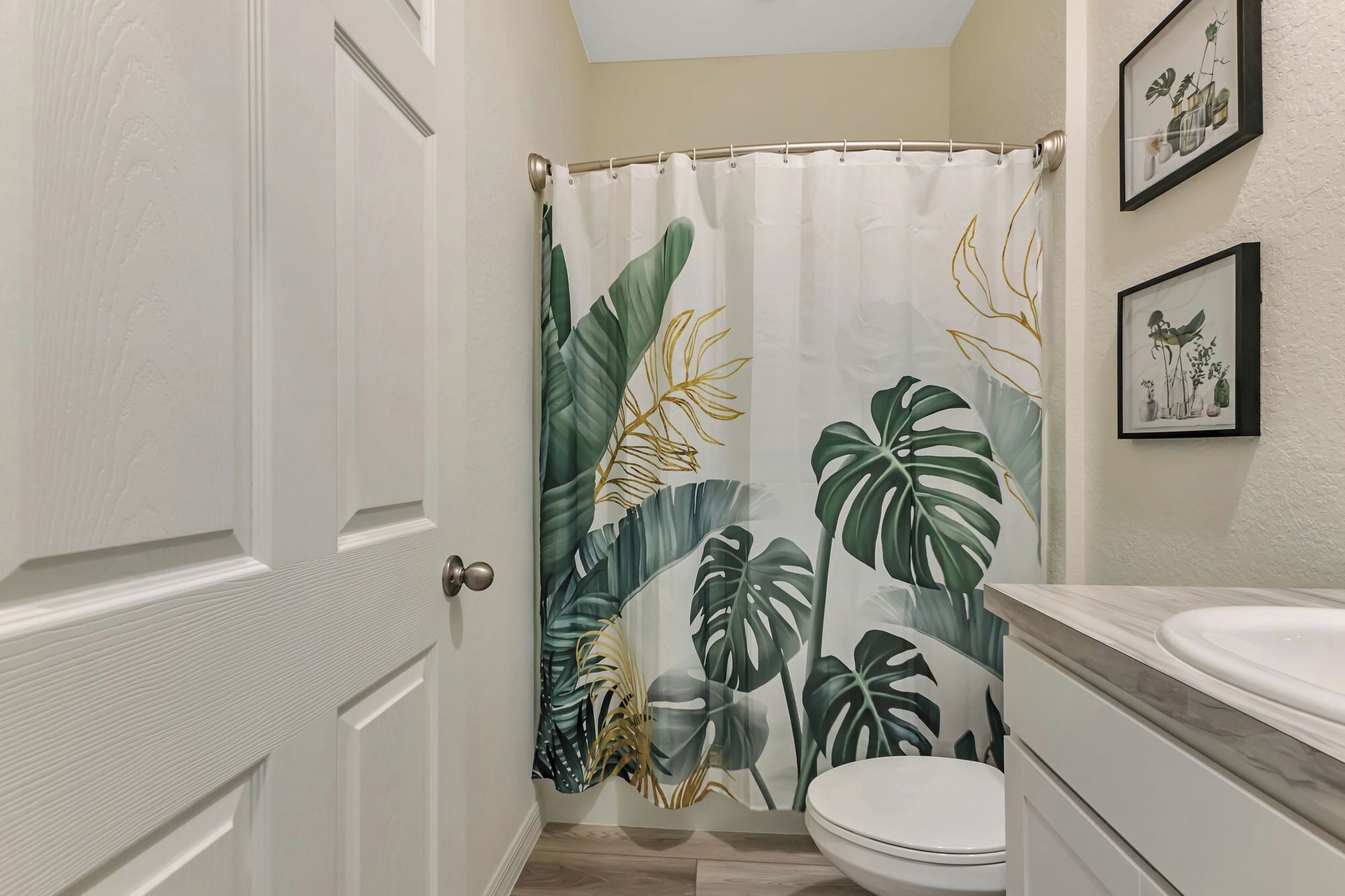 A bathroom with a shower curtain featuring tropical leaf patterns, a white toilet, and a marble sink.