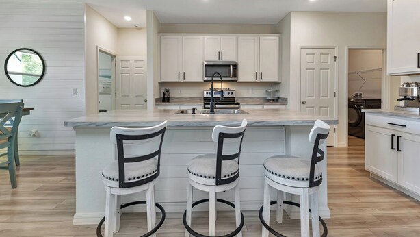 Una cocina moderna con armarios blancos, una isla central con taburetes y un microondas integrado.