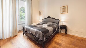 A bedroom with a bed, a window with curtains, a bedside table with a lamp, and two framed pictures on the wall. - Silvy & Paul apartment by MMega (Florence)