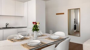 A modern kitchen with white cabinets, a marble countertop, and a dining area with a glass table set for four. - City Center Luxury with AC & Free Parking (Lugano)