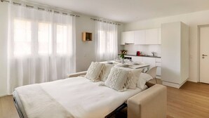 A modern bedroom with a large bed, a bedside table, and a small kitchen area with cabinets and a countertop. - City Center Luxury with AC & Free Parking (Lugano)