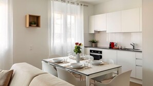 A modern kitchen with white cabinets, a dining table set for four, and a small plant on the counter. - City Center Luxury with AC & Free Parking (Lugano)