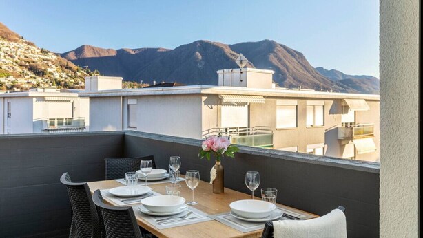A dining table set on a balcony with a mountain view. - City Center Luxury with AC & Free Parking (Lugano)