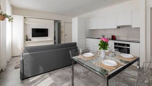 Una cocina moderna con armarios blancos, horno empotrado y comedor con mesa y sillas de vidrio.
