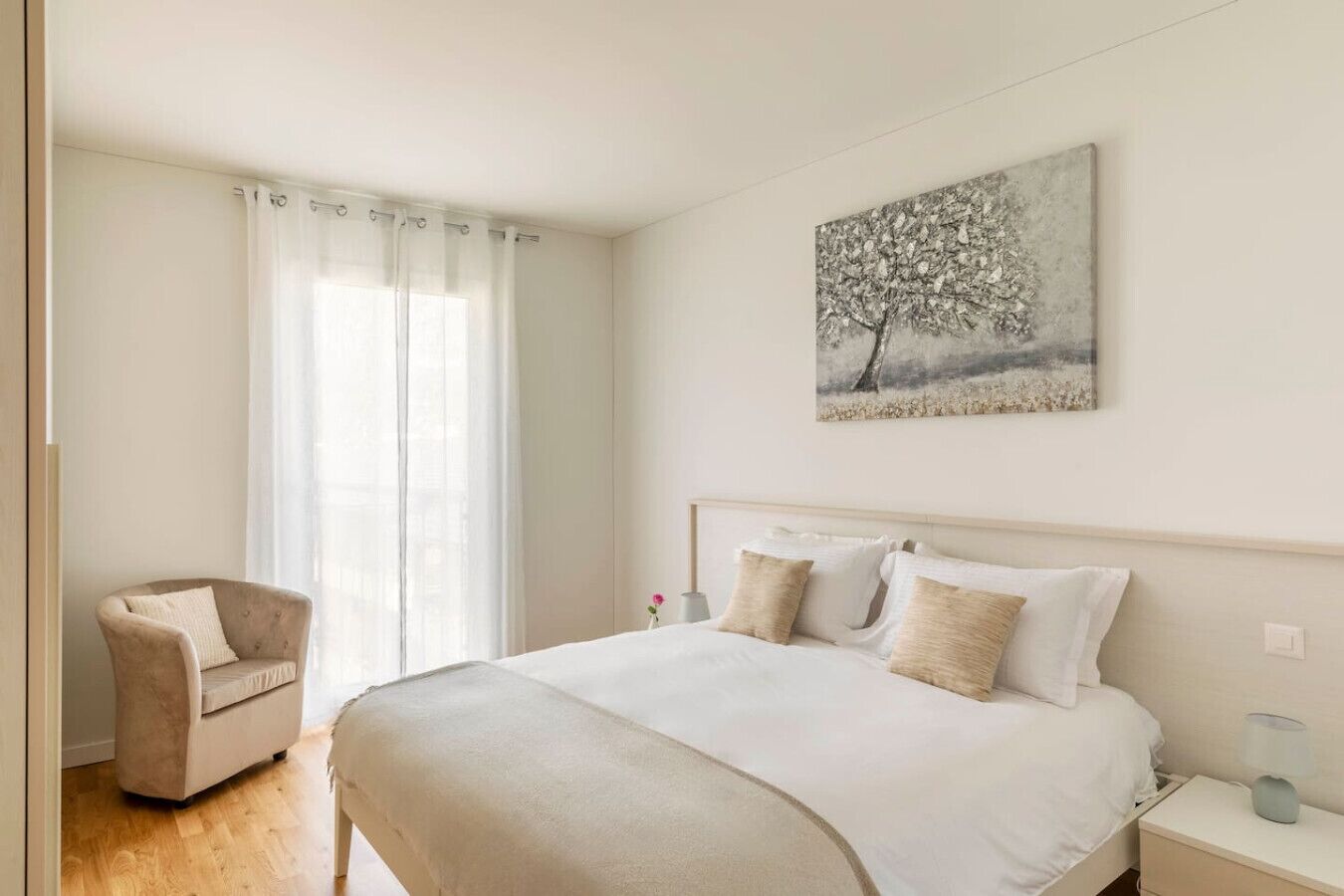 Una camera da letto con un letto, una sedia, un comodino e un quadro appeso al muro.