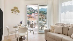 A modern living room with a sofa, a dining table set for two, and a balcony with a city view. - Elegant new Apt with AC, private balcony & garage (Viganello)