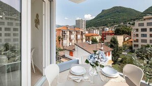 A balcony with a table set for dining, overlooking a cityscape with buildings and a mountain. - Elegant new Apt with AC, private balcony & garage (Viganello)