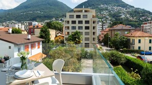 A balcony with a table set for dining, overlooking a residential area with a mountain in the background. - Elegant new Apt with AC, private balcony & garage (Viganello)