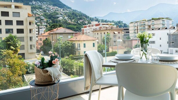 Un balcon avec une table dressée pour le dîner, offrant une vue sur une ville nichée dans les montagnes.