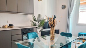 A modern kitchen with grey cabinets, a black oven, and a dining area with a glass table and teal chairs. - Ginevra Suite (Bologna)