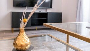 A modern living room with a glass coffee table, a decorative vase with dried plants, a flat-screen TV mounted on the wall, and a dark wooden cabinet. - Ginevra Suite (Bologna)