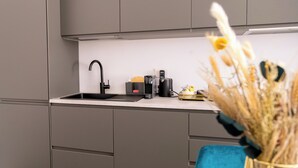 A modern kitchen with grey cabinets, a black faucet, a coffee machine, and a vase with dried flowers. - Ginevra Suite (Bologna)