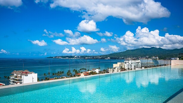 A hotel pool with clear blue water, a view of the ocean, and a mountain in the background. - 1 BR Golden Zone · Luxury Beach and Infinity Pool (Bucerías)